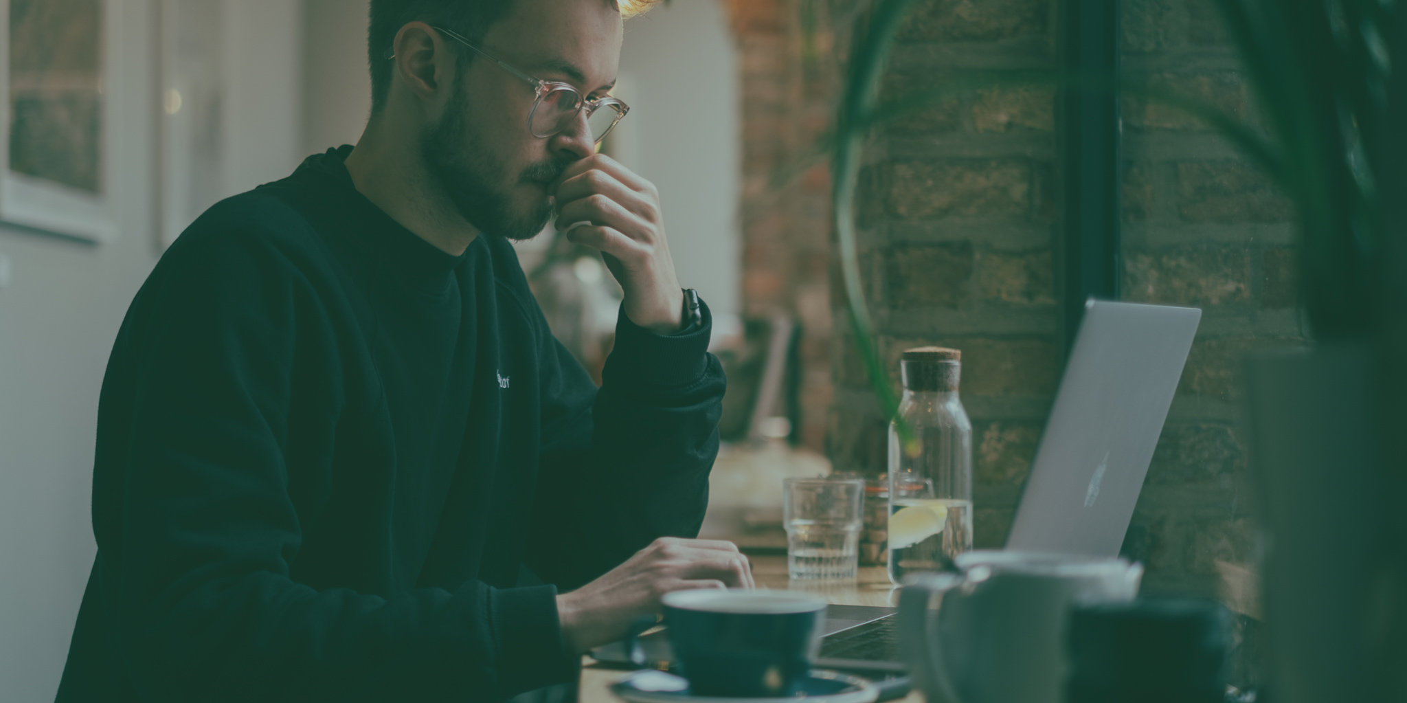 man in a cafe looking at computer and thinking hard